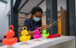 Rashmi, wearing a mask, attempts a steady hand game at Royal Bolton Hospital main entrance, with hook a duck in the foreground