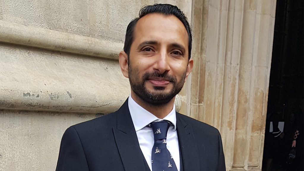 Dr. Rizwan Ahmed MBE in a suit stood outside Westminster Abbey for Queen Elizabeth II's funeral