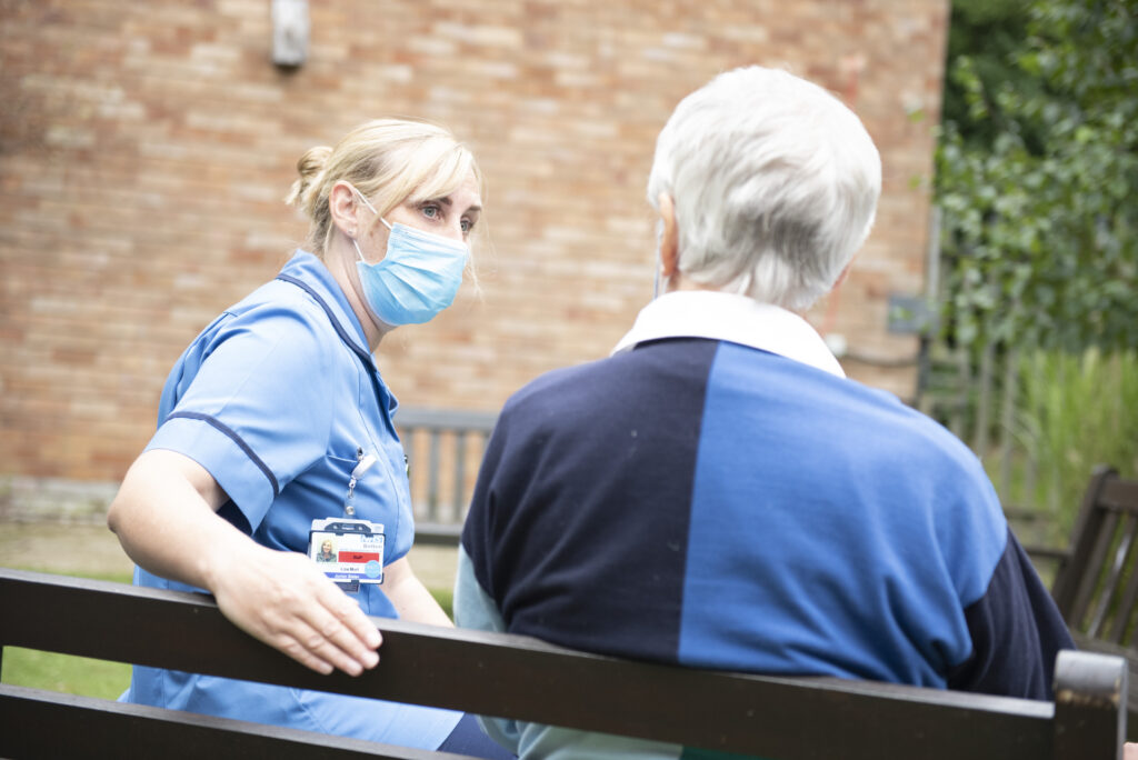 Patients get home sooner, as shown by a nurse speaking to an elderly person on a bench outside