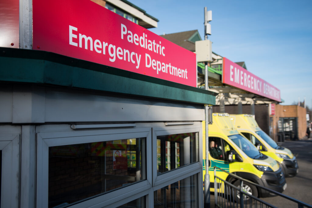 Sign saying paediatric emergency department, with two ambulances in the background