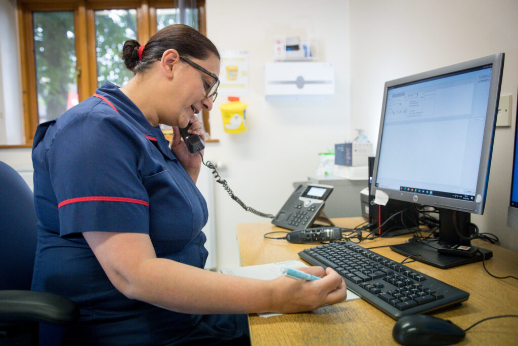 Nurse on phone at desk, with computer in front of her