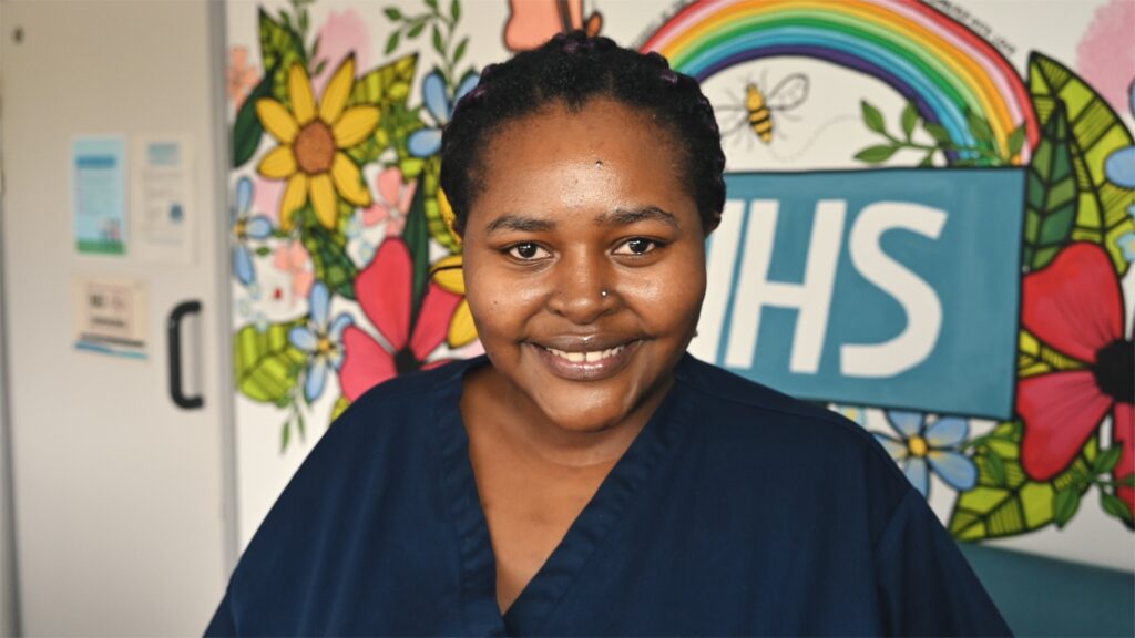 Member of staff wearing uniform smiles for a picture in front of wall mural