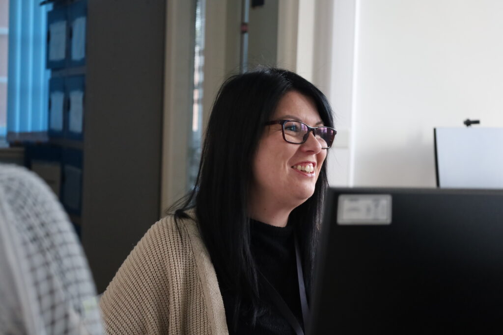 Rebecca sits at her desk at Farnworth Town Hall, smiling to colleagues