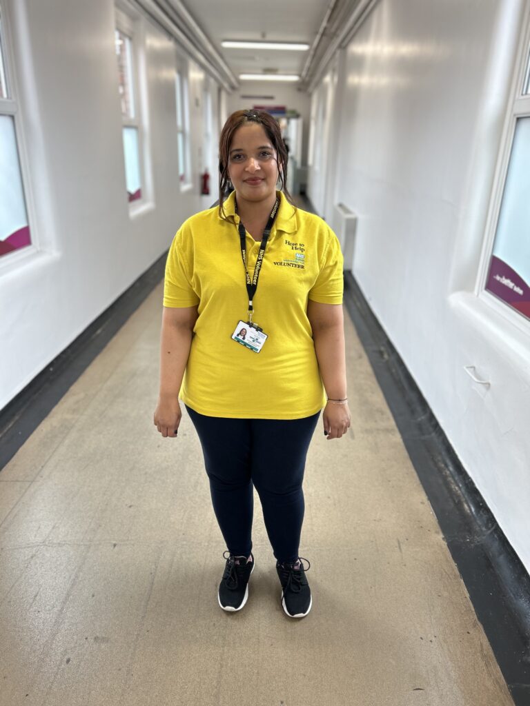 Volunteer Mansha Shaikh smiles for a photo in her bright yellow volunteers uniform